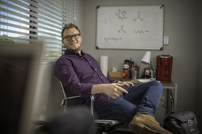 A student sits in their dorm room with equations written on the whiteboard behind them.