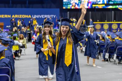 An NAU graduate student smiles and celebrates with her diploma during commencement.