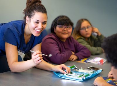 An NAU Dental Hygiene student shows young students the different dental tools they practice with.