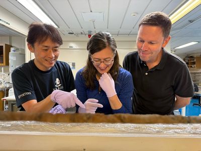 Christine Regalla, center, looking at a table of sediment with nitrile gloves on surrounded by two other researchers