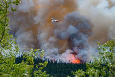 Emergency helicopter flying above a forest fire and billowing smoke