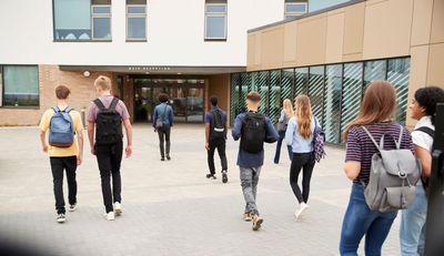 Teenagers with backpacks walking toward a school entrance