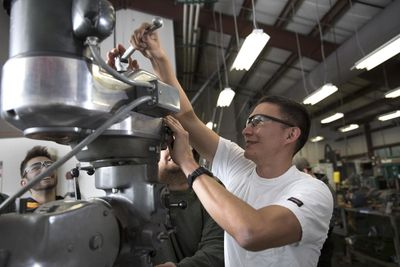 A student wears protective goggles and works with mechanical engineering equipment.
