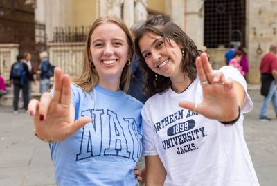 Two student are smiling for the camera and holding up the Jacks hand sign.