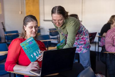 Students work on a laptop and hold a Thin Air magazine book.